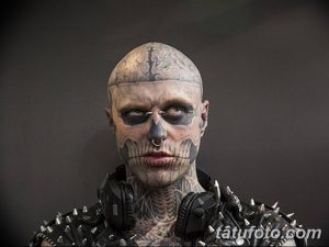 Фото тату: мужчина с татуировкой черепа, полностью покрывающей его лицо, с черными наушниками.